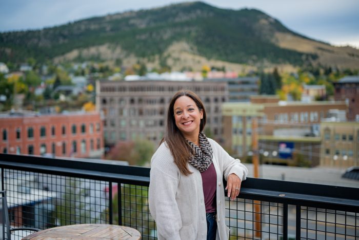 Alani Bankhead leaning on a rooftop railing above a Montana downtown with a mountain behind her.