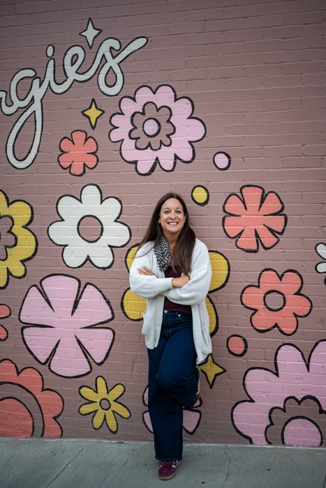 Full-length vertical photo of Alani Bankhead in front of a pink flower mural.