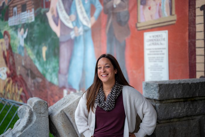 Alani Bankhead smiling in front of the Women&rsquo;s Commemorative Mural, wider frame.