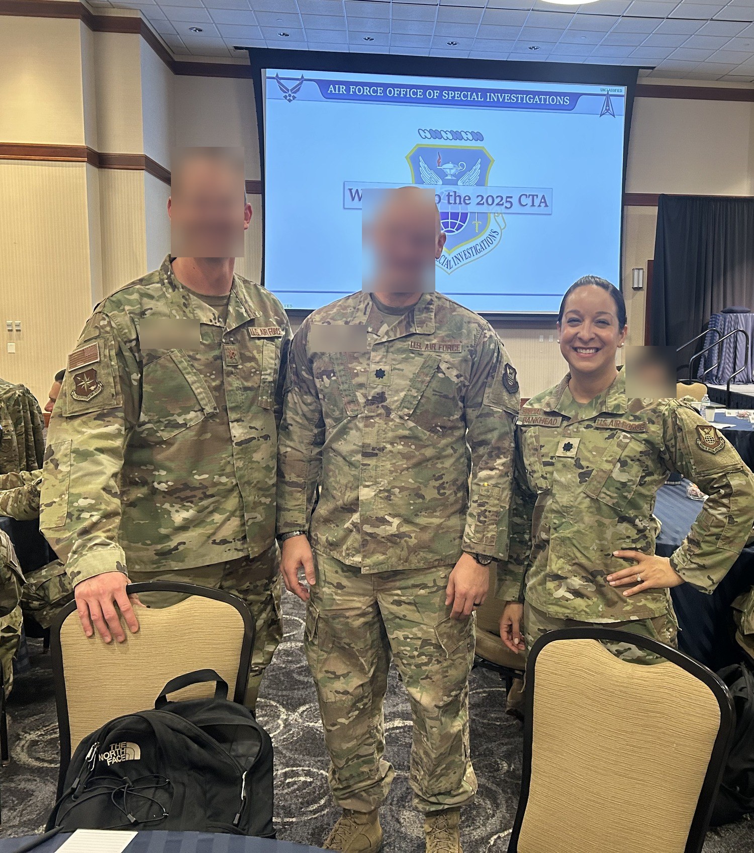 Alani Bankhead in uniform with two other officers at the 2025 Air Force Office of Special Investigations Commander's Training Alignment conference, the OSI seal and organization name on the screen behind them.