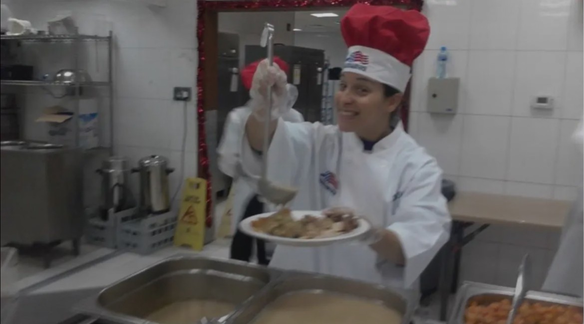 Alani Bankhead in a chef coat and hat, plating food on the serving line at the deployed holiday meal.
